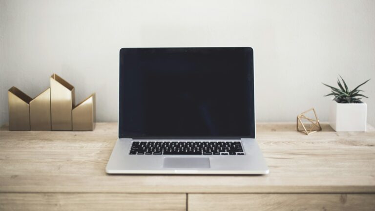 Laptop na drewnianym biurku obok notesu i rośliny